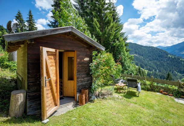 Freistehende Holzsauna im Garten mit Liegestühlen und Bergblick