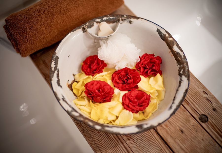Schale mit roten Blüten und Badeutensilien neben der Badewanne
