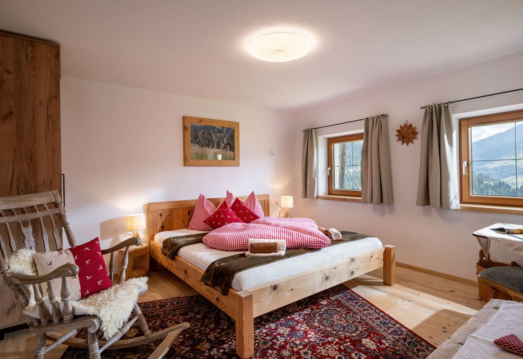 Schlafzimmer mit Doppelbett, Holzmöbeln und zwei Fenstern mit Bergblick